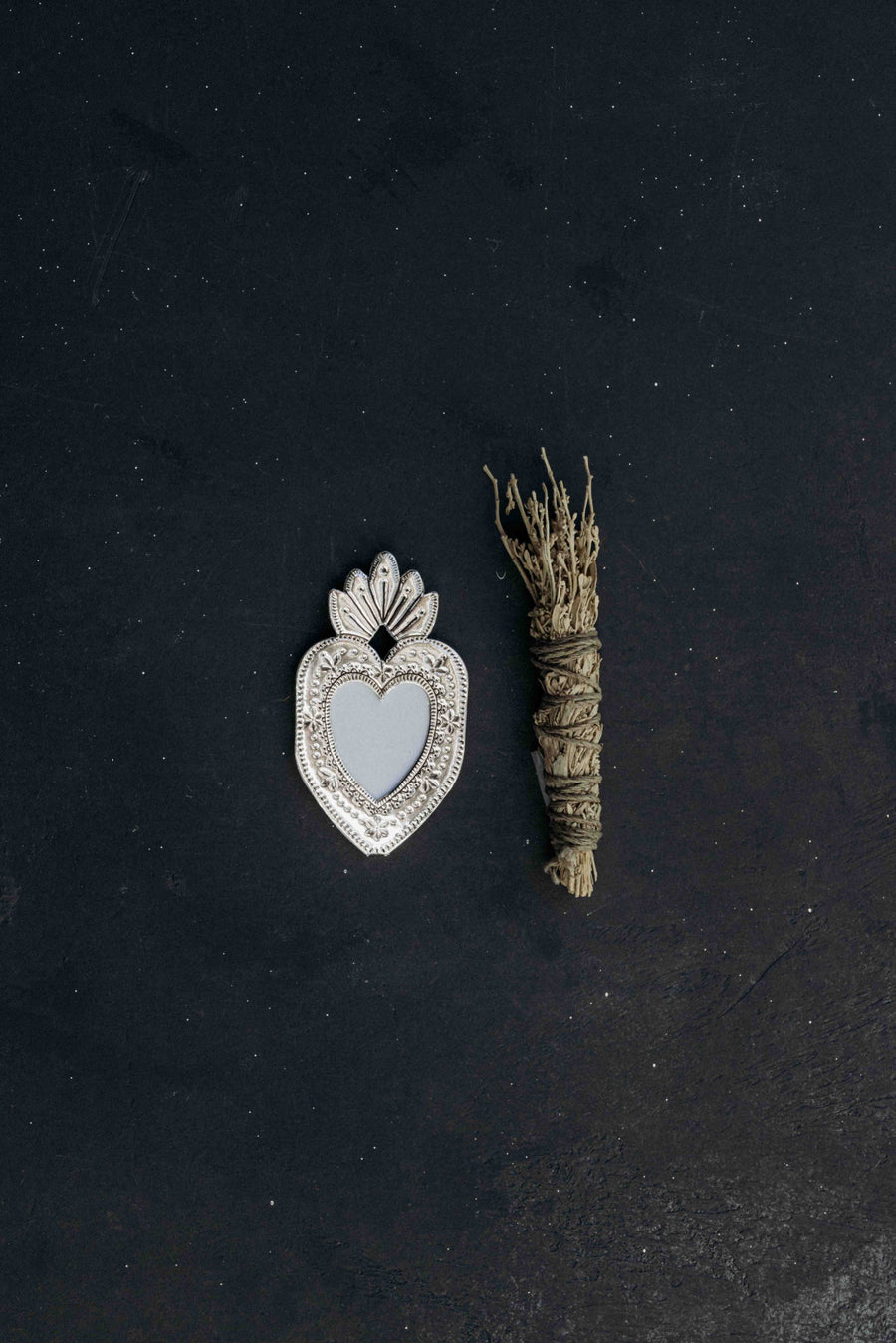 Heart-shaped silver pendant and dried plant on a black background
